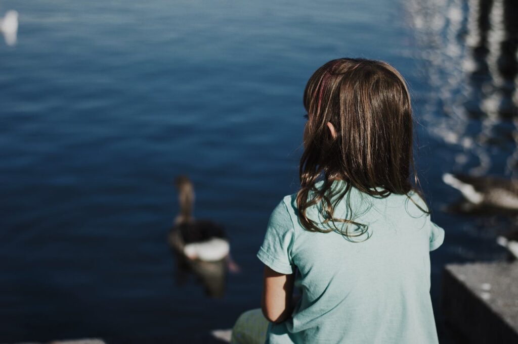 Oser être différent : l'allégorie du vilain petit canard (image décorative d'une petite fille de dos assise face à un lac en train d'observer un canard en train de s'éloigner)